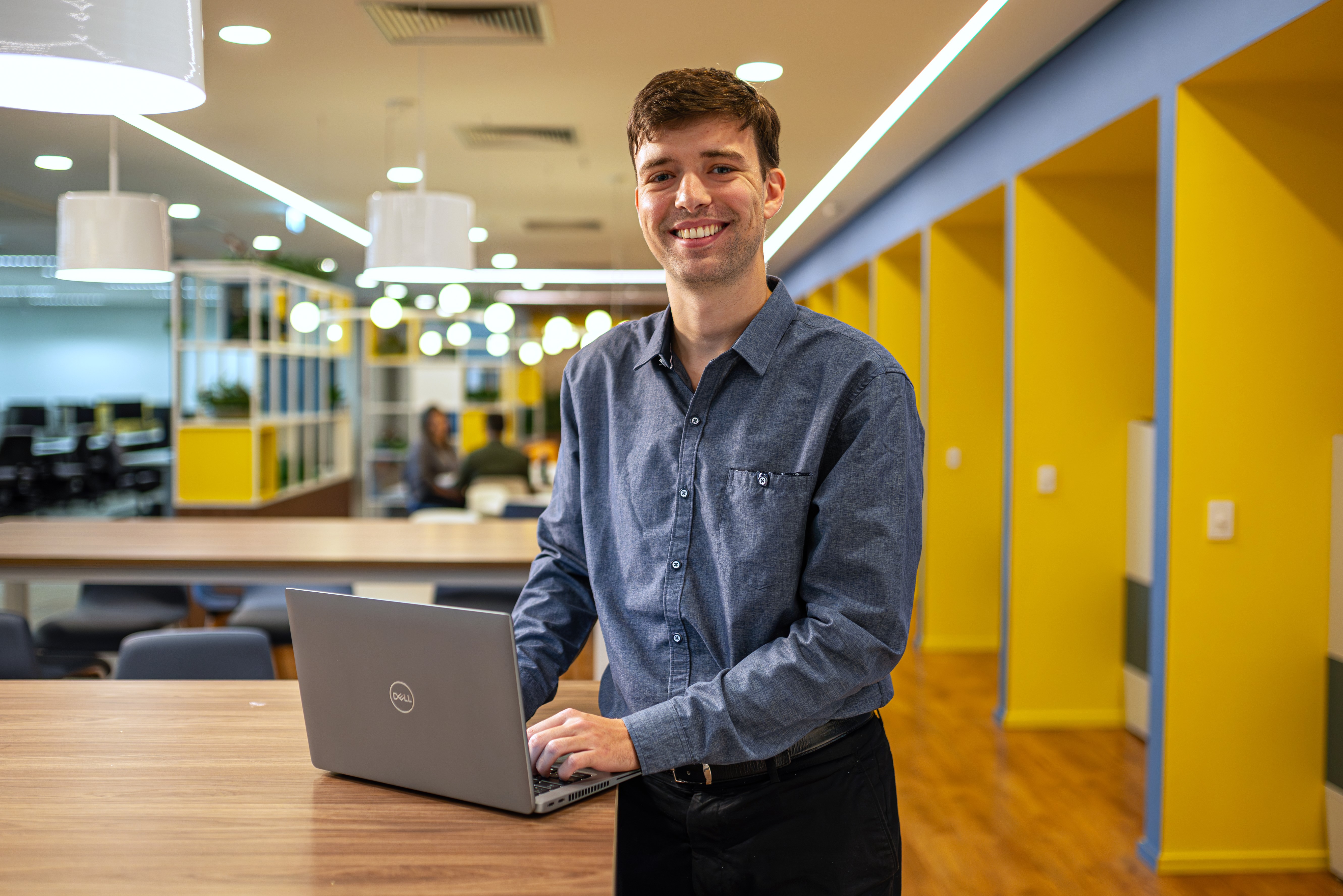 Luca smiles while standing next to a table with an open laptop.