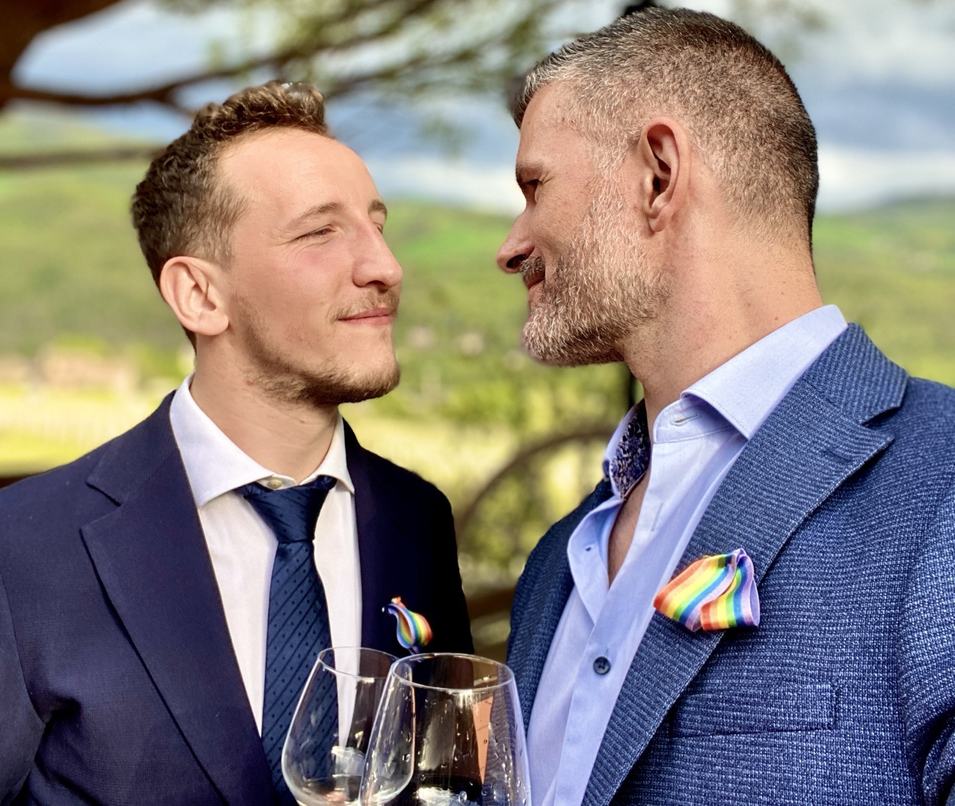 Stevo and his husband wearing suits and holding wine glasses.