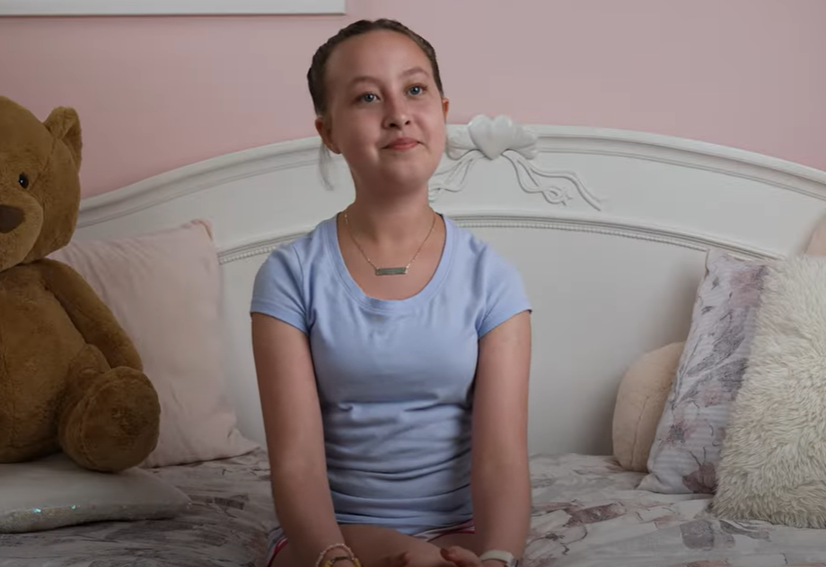 Girl, Izzy, sits on her bed