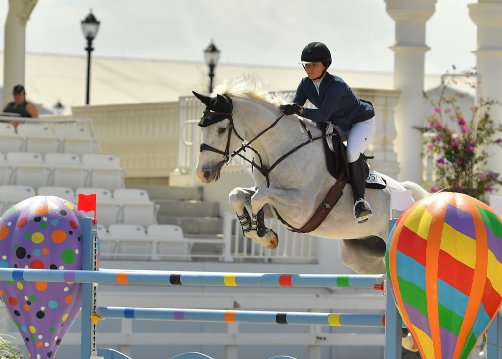 Catherine goes over a jump on a white horse.